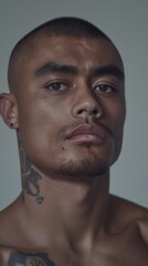 Obraz premium A Pacific Islander man poses confidently, revealing detailed tattoos under soft lighting that highlights his strong features