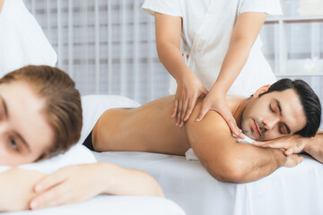 Caucasian couple customer enjoying relaxing anti-stress spa massage and pampering with beauty skin recreation leisure in day light ambient salon spa at luxury resort or hotel. Quiescent