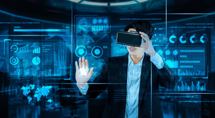 Project manager with VR goggles pointing financial chart and glowing blue light at office. Skilled...
