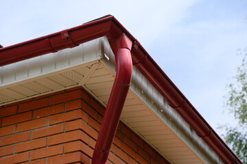 Rain gutter from the roof of red brick house. Metallic guttering system.