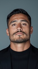 Obraz premium A Hispanic man stands confidently in a casual black outfit, showcasing his strong features against a simple background