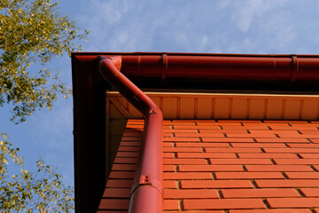 Rain gutter from the roof of red brick house. Metallic guttering system.
