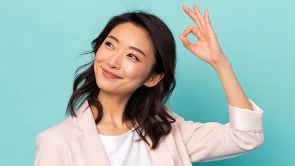 Fototapeta premium a young woman with long black hair wearing a white t-shirt and a pink blazer smiling and making an okay gesture with her hand. She looks confident and happy, with a radiant smile.