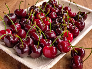 Wooden plate with fresh cherries, close up, studio shot
