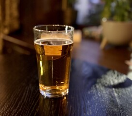 An unfinished transparent glass mug with light beer and foam on the bar in an elite pub. Close-up