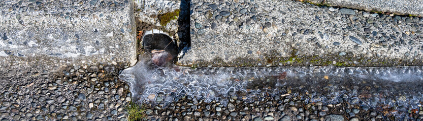 Stormwater outflow from residential yard on a frozen sunny winter day, ice remaining on street...