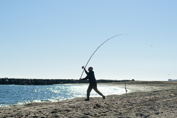 Fisherman casting fishing rod from shore on sunny day