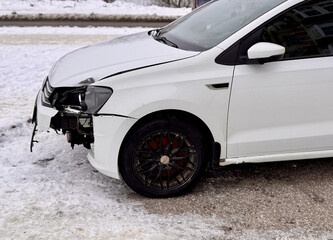 This detailed image depicts a closeup view of a damaged white car sitting in a snowy winter...