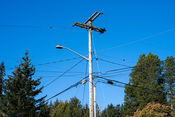 Wooden telephone and power line utility pole, including LED streetlight, against a sunny blue...