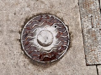 A dirty rusty iron hatch with a pattern is located next to dry grass during the daytime
