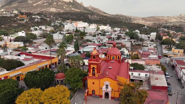 Colourful parish with Pe&ntilde;a de Bernal in the background in Mexico. Drone descends on the church and tilts to reveal the rock in the background