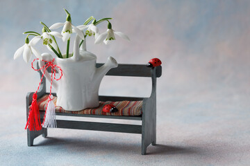 Card for the holiday of March 1, Martisor, Baba Marta. Decorative bench with a watering can, a bouquet of snowdrops, red and white symbol of Martenitsa, copy space