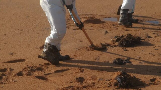 Emergency workers clean the beach after an rude oil spill with a shovel in protective clothing. Pollution due to the petroleum tanker accident