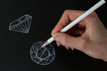 The work of a jeweler-designer. A jewelry designer develops sketches of jewelry.  Sketching precious stones with a white pencil on a black background. Design studio. Creative ideas.