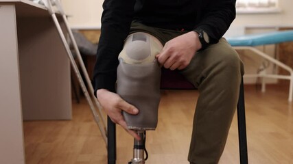Prosthetic leg, adjusting prosthetic, rehabilitation center. Close-up man adjusting his prosthetic leg while seated in rehabilitation center, setting includes medical tools and support equipment