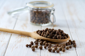 allspice or Jamaican pepper in a wooden scoop and in glass storage jar on a white wooden table,...