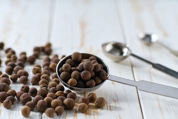 allspice or Jamaican pepper seeds in a measuring spoons on a white wooden table, selective focus.