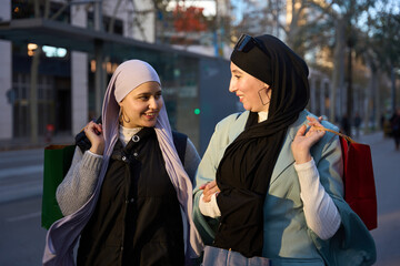 Two muslim women wearing hijab are walking and talking after shopping