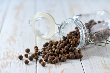 allspice or Jamaican pepper spill out of a glass storage jar on a light kitchen table, selective focus.