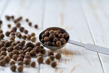 allspice or Jamaican pepper spilled from a teaspoon on a light kitchen table, selective focus.