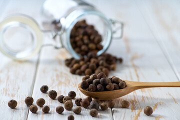 allspice or Jamaican pepper in a wooden scoop and in glass storage jar on a light kitchen table, selective focus.