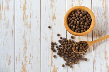 allspice or Jamaican pepper in a wooden bowl on a light kitchen table, top view.