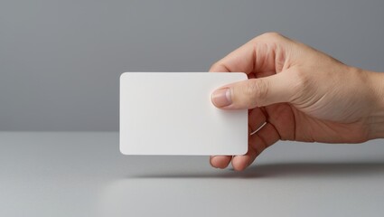 Hand holding blank white business card mockup on gray background