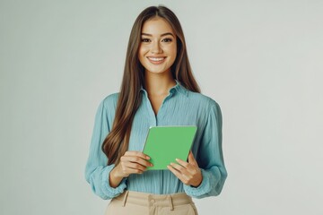 Smiling Woman Holding Tablet with Green Screen on Light Blue Background. Confident woman in a blue blouse holding a tablet with a green screen, standing against a light blue background, i