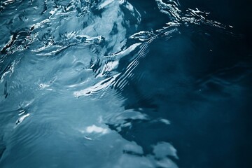 Abstract close-up of dark blue water surface with ripples and reflections.