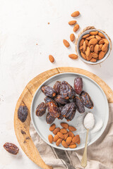 Medjool dates and almonds on a gray plate with a spoonful of shredded coconut, placed on a wooden board with a beige cloth in the background. Top view