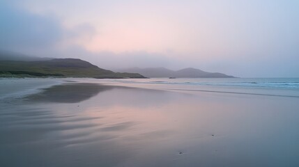 A serene beach scene at dawn, featuring gentle waves lapping against the shore with misty mountains in the background.