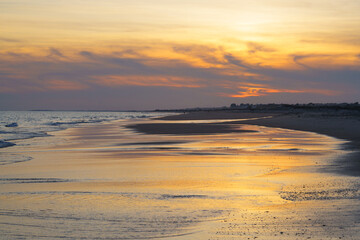 Tranquil shoreline bathed in warm hues as the sun sets over the ocean.