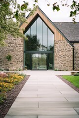 Fototapeta premium A contemporary stone house featuring expansive windows is nestled in a peaceful neighborhood, adorned with beautiful gardens and a charming pathway, all under a serene cloudy sky