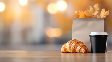 Warm Croissant and Coffee Cup on Wooden Table with Blurred Autumn Background and Paper Bag with Leaves
