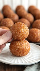 Crispy Rice Balls: Close-up shot of two crispy rice balls, one stacked atop the other, held by a hand, with a background of additional rice balls arranged on a baking sheet, a delicate white plate.