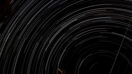 A hypnotic star trail background swirls in long exposure, forming intricate celestial patterns. The...
