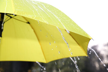 Open yellow umbrella under pouring rain outdoors, closeup