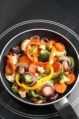 Frying pan with mix of vegetables and mushrooms on cooktop, top view