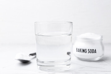 Glass of water and baking soda on white textured table, selective focus