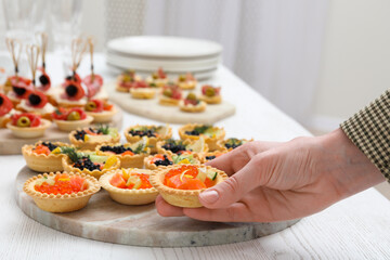 Woman taking tasty canape at white wooden table, closeup