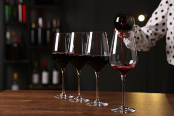 Professional sommelier pouring red wine into glasses at wooden table indoors, closeup