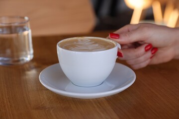 Woman with cup of aromatic coffee at wooden table in cafe, closeup
