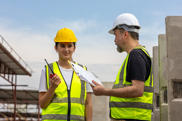 A male engineer gives safety advice to his female trainee in a floor making factory. Senior supervisor discusses with his assistant or clerk checking the concrete wall production system