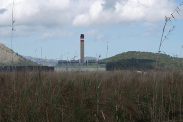 View of Es Murterar thermal power station or Alcudia power station, mountains and nature on cloudy day from hiking trail in Albufera de Alcudia, Mallorca, Balearic Islands. Natural reserve park.