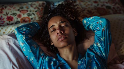Fototapeta premium Sick biracial woman wearing blue pyjamas touching her head in bedroom 
