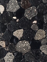 Black rock surface with a detailed texture, featuring small white spots of lichen and scale on the surface. The rocks have straight horizontal lines that give it an abstract feel.