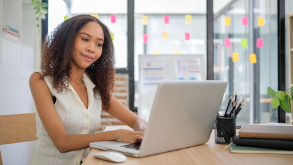 Smiling African American businesswoman working with laptop at modern workplace.