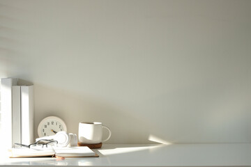 Minimalistic workspace featuring a white desk with books, a coffee mug, glasses, headphones, and a clock.