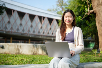 Relaxed student working on her laptop in a tranquil campus environment, combining productivity and nature.