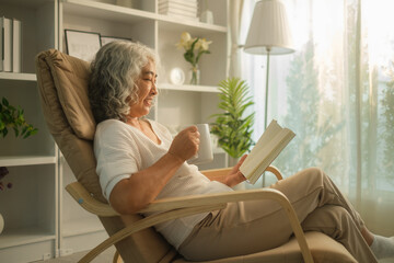 Relaxed senior woman drinking hot tea and reading book on armchair in cozy living room.